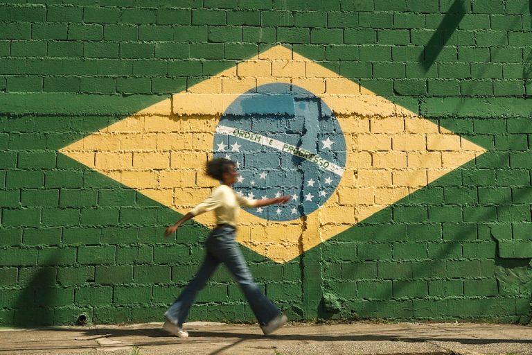 Mulher passando em frente a bandeira do Brasil pintada em muro