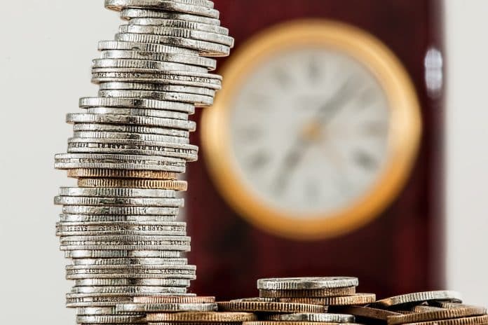 Pilha de moedas com relógio ao fundo
