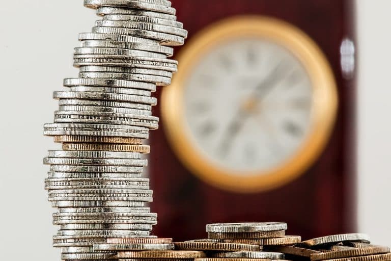 Pilha de moedas com relógio ao fundo