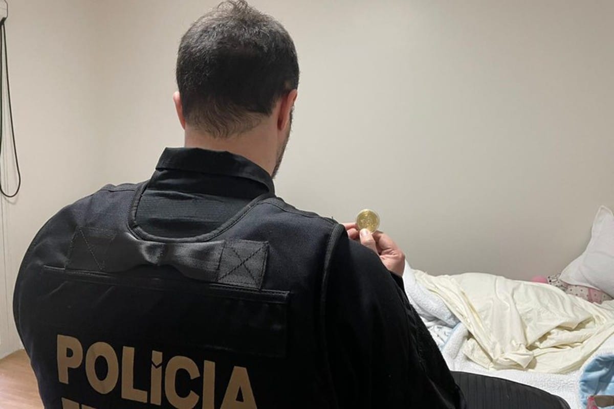 Agente da PF segurando bitcoin simbólico