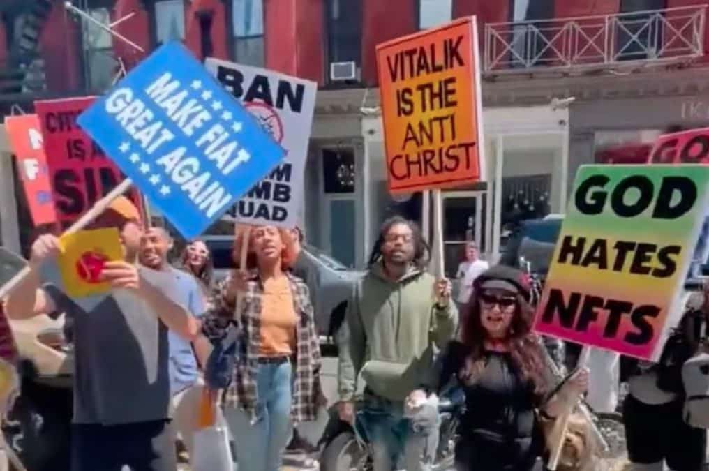 Protestantes segurando cartazes com dizeres “Deus odeia NFTs” e “Vitalik [Buterin] é o Anti-Cristo”.