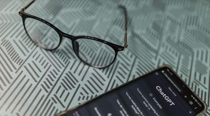 Óculos em mesa de ferro ao lado de celular com imagem do ChatGPT