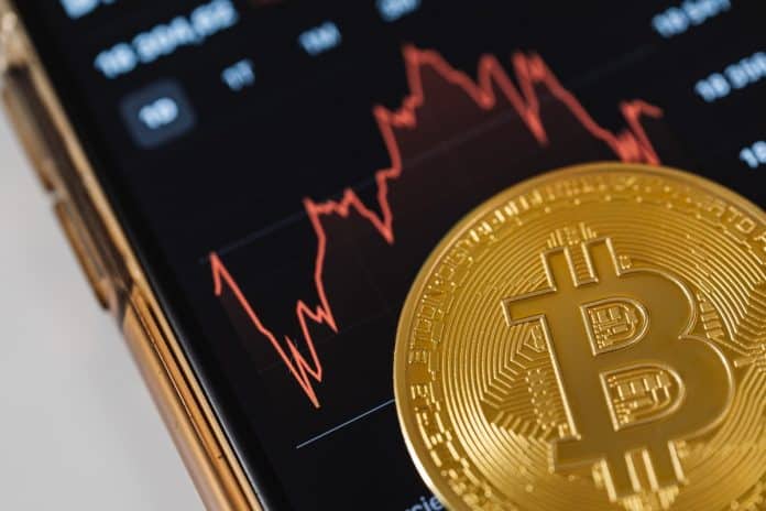 Tela de celular com gráfico em queda e bitcoin na frente