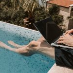Pessoa usando computador na beira da piscina. Foto de Vlada Karpovich/Pexels.