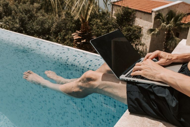 Pessoa usando computador na beira da piscina. Foto de Vlada Karpovich/Pexels.