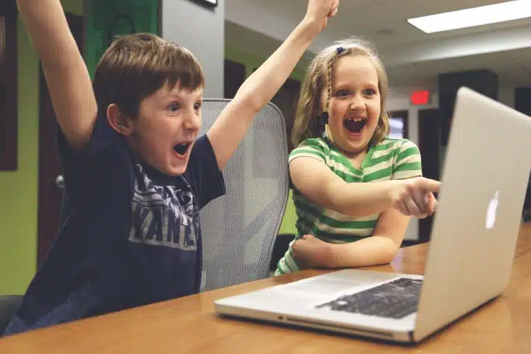 Crianças comemorando ao olhar para tela de notebook