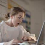 Mulher atenta ao computador e entusiasmada com o que está vendo binance criptomoedas curso