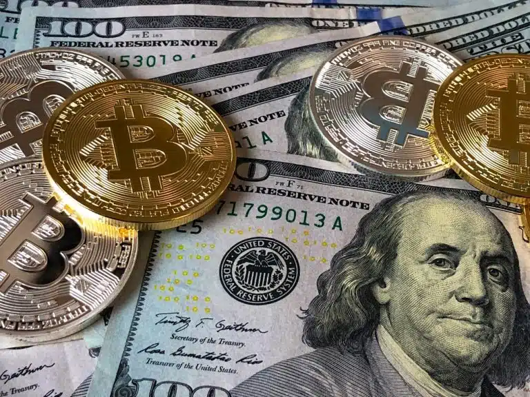 Moedas simbólicas de Bitcoin com notas de Dólar ao fundo