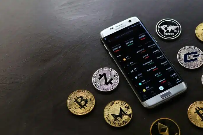 Celular com aplicativo do CoinMarketCap ao lado de criptomoedas simbólicas