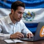 Homem mexendo em computador com símbolo do bitcoin e bandeira de El Salvador ao fundo