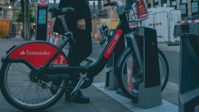 Mulher segurando bicicleta na rua com símbolo do Santander