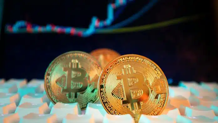 Bitcoin sobre teclado com gráfico de negociações ao fundo