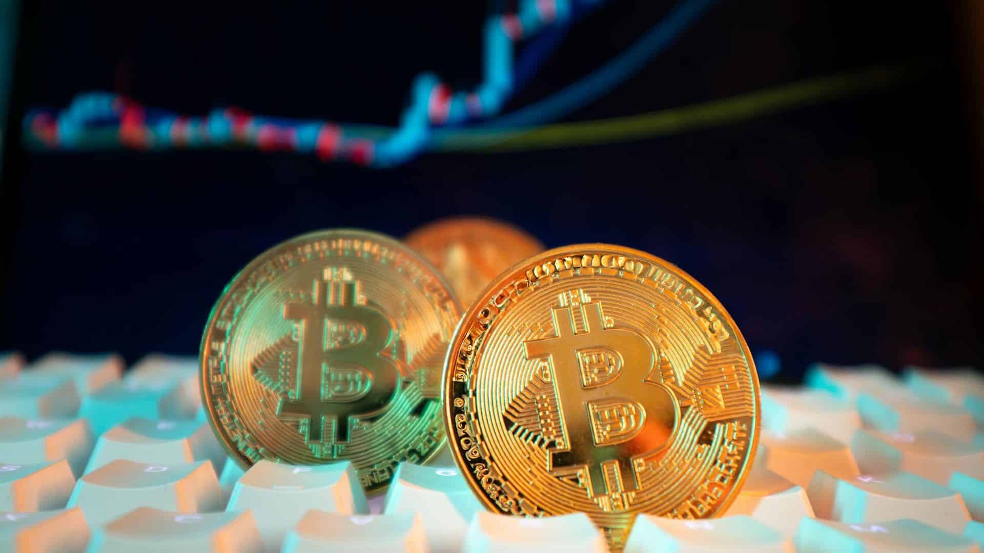 Bitcoin sobre teclado com gráfico de negociações ao fundo