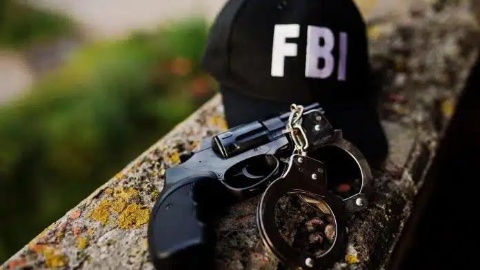 Boné com escrita FBI próximo de revólver e algemas criptomoedas