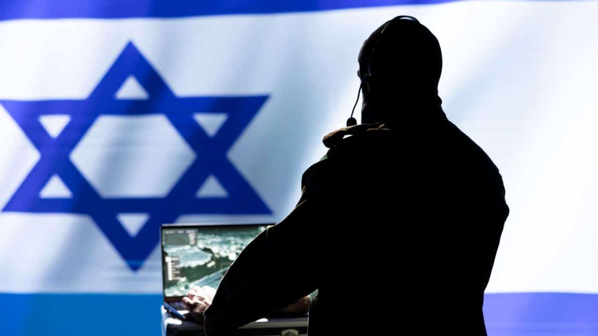 Homem com computador ligado em frente a bandeira de Israel criptomoedas Irã