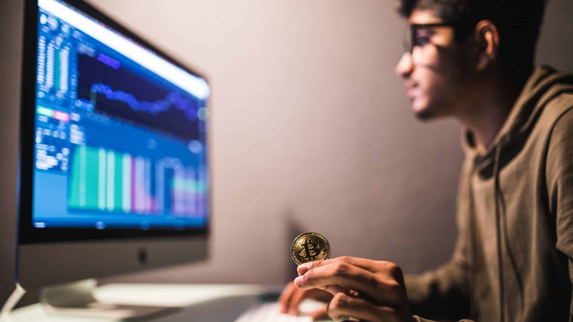 Investidor segurando bitcoin ao analisar gráficos na Binance trader