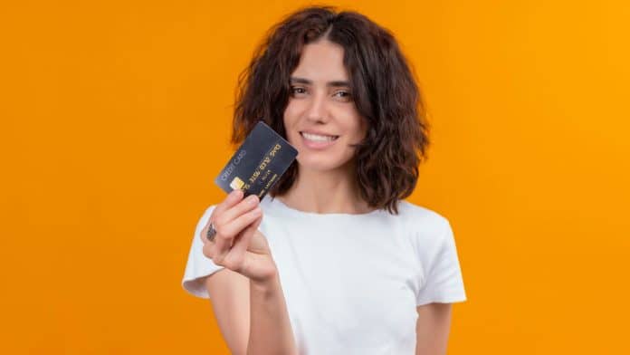 Mulher segurando cartão com fundo laranja banco do brasil brasileira criptomoedas