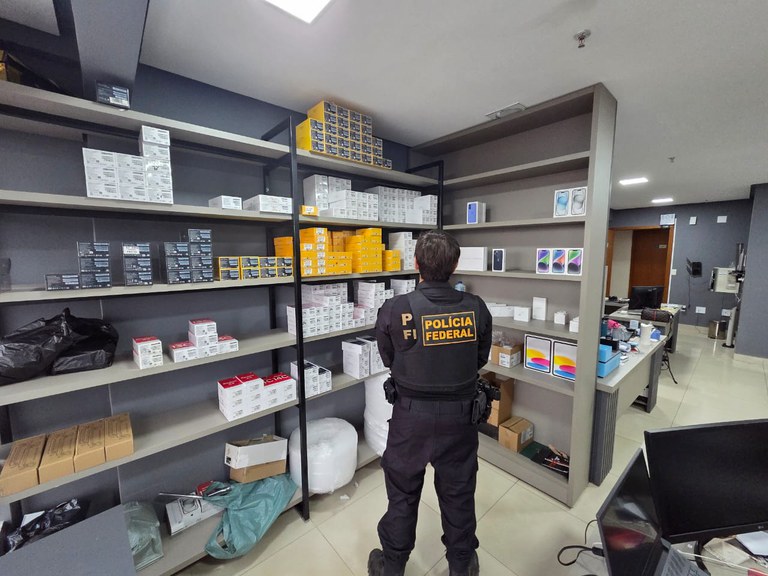 Agente da PF observa eletrônicos apreendidos de suspeitos