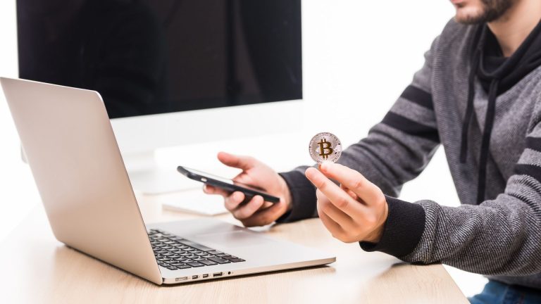 Homem segurando bitcoin enquanto opera no mercado