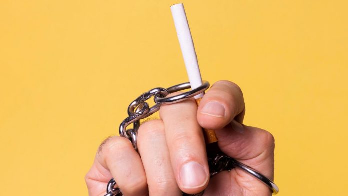 Mão acorrentada ao segurar um cigarro criptomoedas golpista