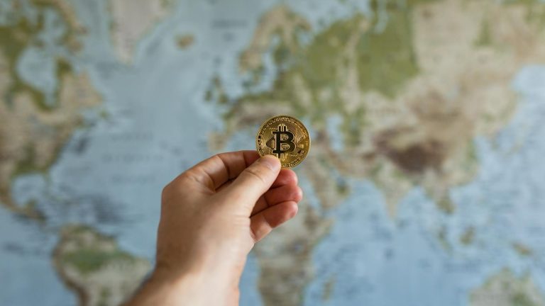 Mão segurando bitcoin na frente de um globo terrestre ministério público