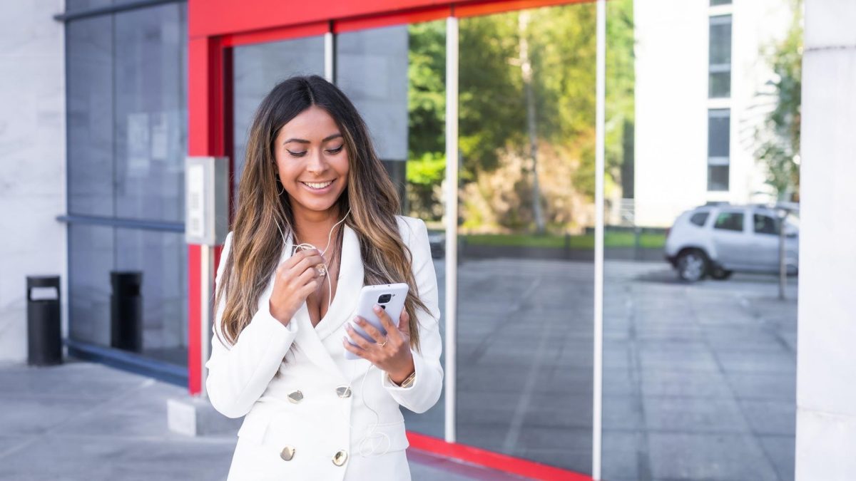 Mulher sorrindo na porta de agência bancária com fachada vermelha Santander Brasil criptomoedas