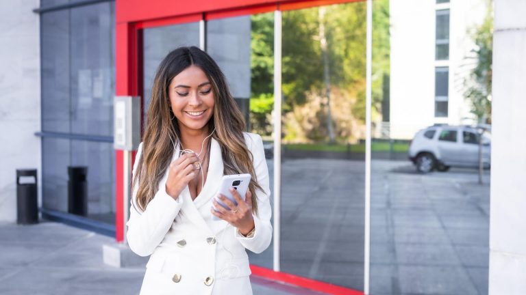 Mulher sorrindo na porta de agência bancária com fachada vermelha Santander Brasil criptomoedas