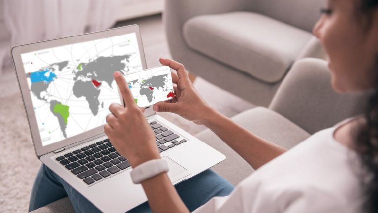 Mulher tirando foto de tela de computador Cloudfare Radar divulga os serviços de criptomoedas mais acessados no ano de 2025 no mundo todo