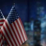 Bandeira dos Estados Unidos em destaque com prédios ao fundo FBI revela perdas bilionárias com fraudes com criptomoedas e alerta investidores sobre táticas de inteligência artificial