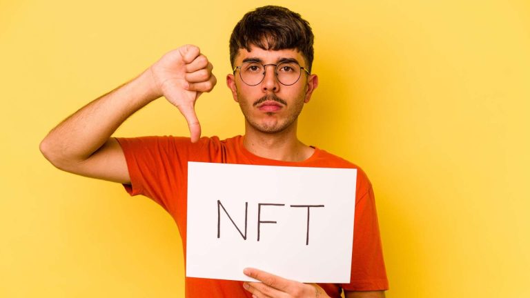 Homem com placa escrita NFT e apontando dedo para baixo em sinal pessimista Plataforma de NFTs encerra operações, culpa mercado e alerta colecionadores sobre obras