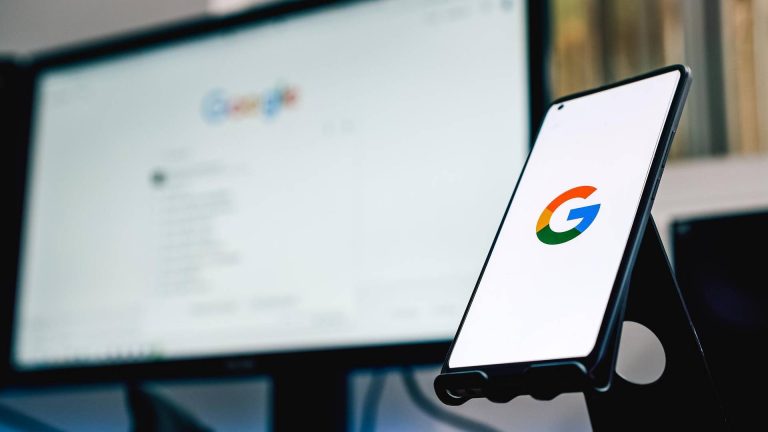 Google Finanças atualiza no Brasil com novas opções para investidores de criptomoedas Símbolo do Google em smartphone e computador ao fundo