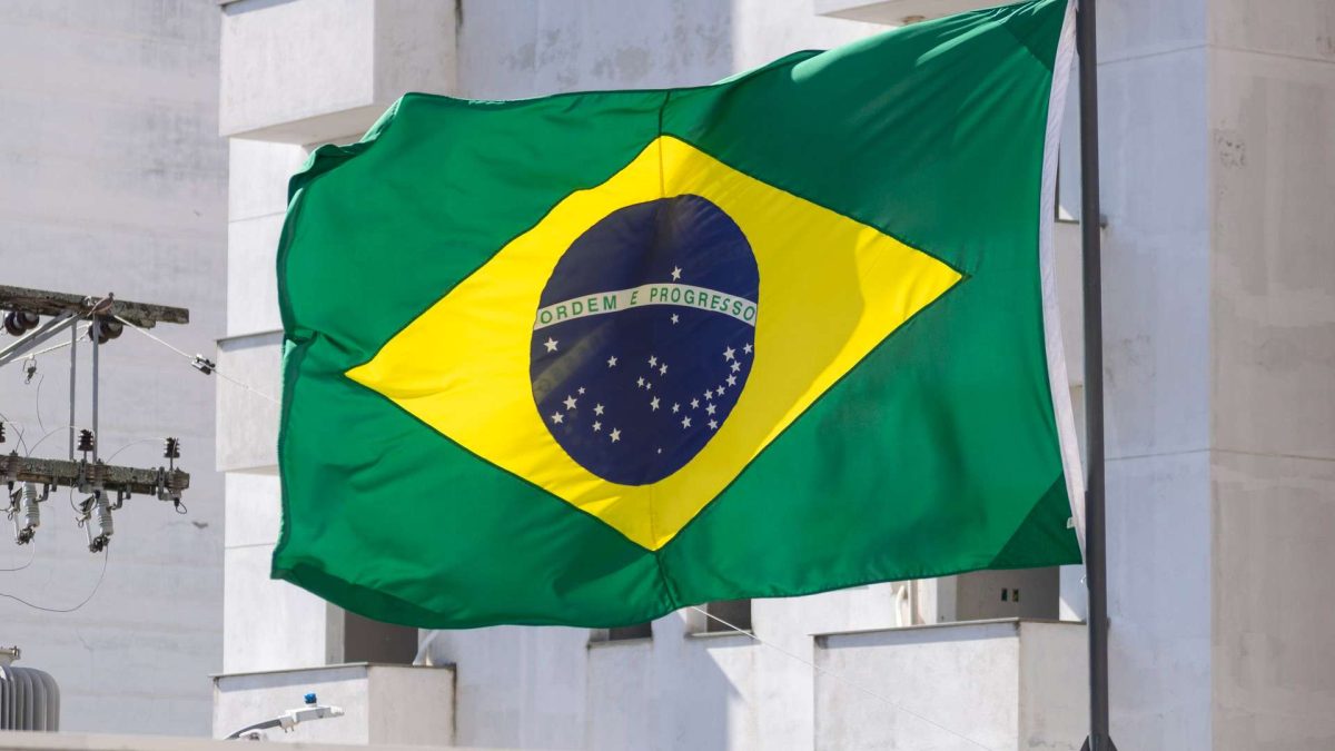 Bandeira do Brasil com prédio branco com fundo Novos decretos ampliam exigências para empresas digitais e repercutem no mercado cripto e em negócios baseados em blockchain