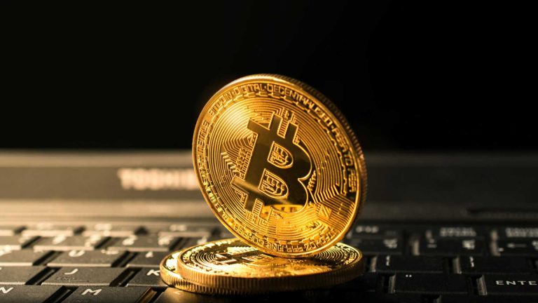 Bitcoin sobre computador apontando para baixo