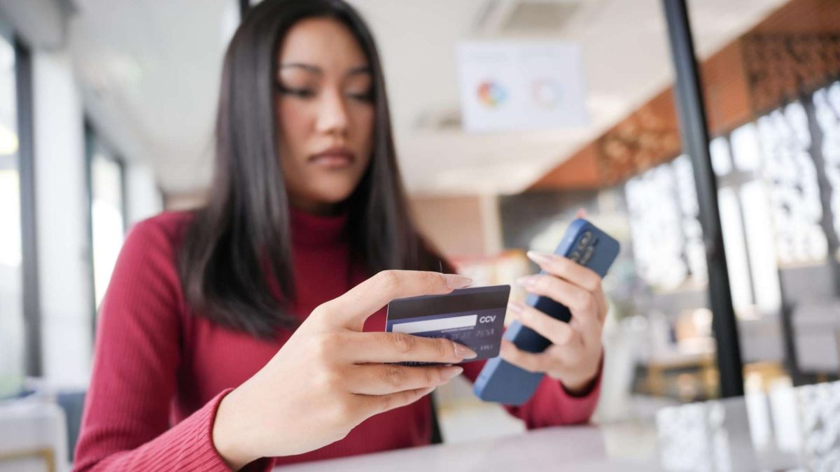 Mulher com cartão de banco e celular na mão Santander vai liberar criptomoedas para todos os seus clientes no Brasil, veja lista dos ativos