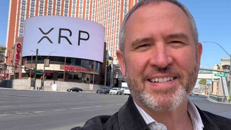 Brad Galinghouse com símbolo do XRP em prédio ao fundo CEO da Ripple critica Michael Saylor por sua estratégia de comprar bitcoin toda semana