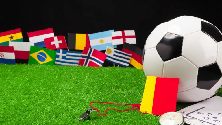 Campo de futebol com bandeira das seleções ao fundo, em Copa do Mundo