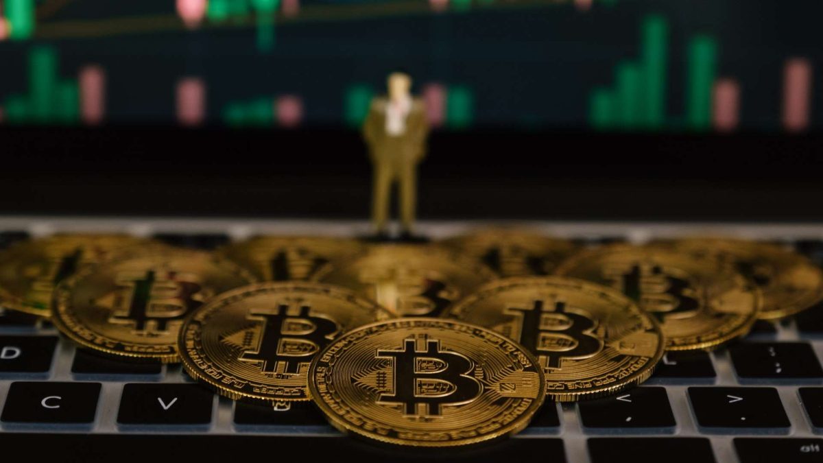 Gráfico do bitcoin com moedas simbólicas sobre mesa e miniatura de executivo observando Companhia brasileira compra 41 bitcoins e supera 3.800 unidades em sua posse