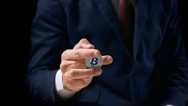 Homem de terno segurando bitcoin entre dedos da mão Ministério Público treina servidores para rastrear crimes com criptomoedas no Mato Grosso do Sul
