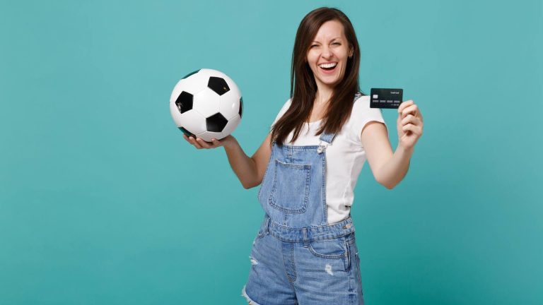 Mulher com cartão na mão e bola na outra Brasileiros gastaram mais de US$ 2,4 milhões nos países-sede da Copa do Mundo durante o mês com o Cartão OKX