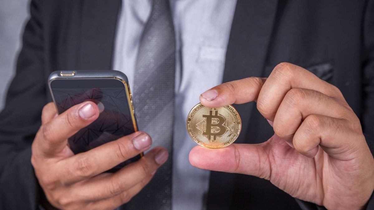 Executivo com bitcoin na mão e celular na outra