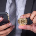 Executivo com bitcoin na mão e celular na outra
