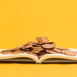 Livro com moedas em cima e fundo amarelo