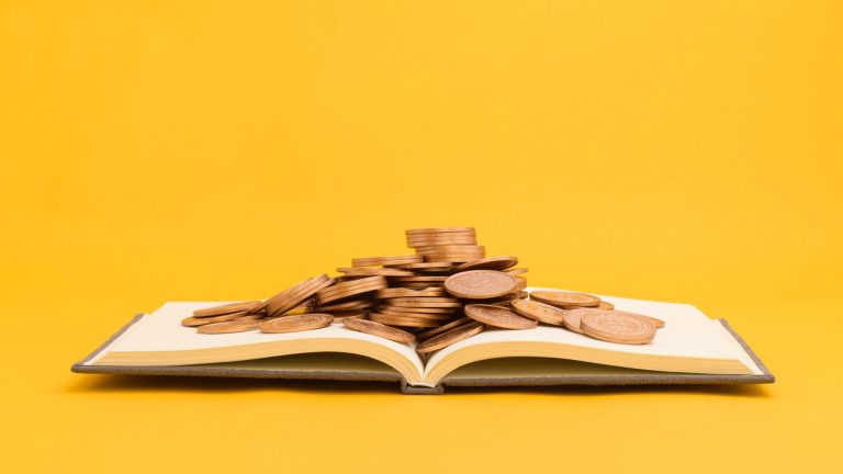 Livro com moedas em cima e fundo amarelo