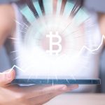 Mulher com símbolo do bitcoin brilhando em celular Mais um ataque hacker a empresa de bitcoin, agora no BTCPay Server, que pede atualização urgente a usuários