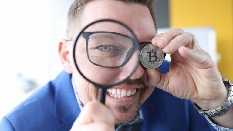 Homem sorrindo com lupa na mão e bitcoin na outra MP de SC busca corretoras de criptomoedas para guardar fundos apreendidos de graça