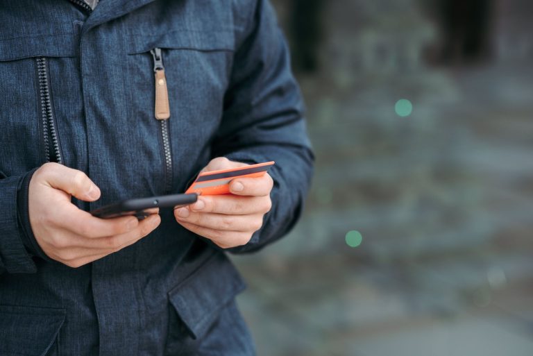 Pessoa com cartão de banco e celular em mãos