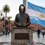 Estátua fictícia de Satoshi Nakamoto com bandeira da Argentina ao fundo