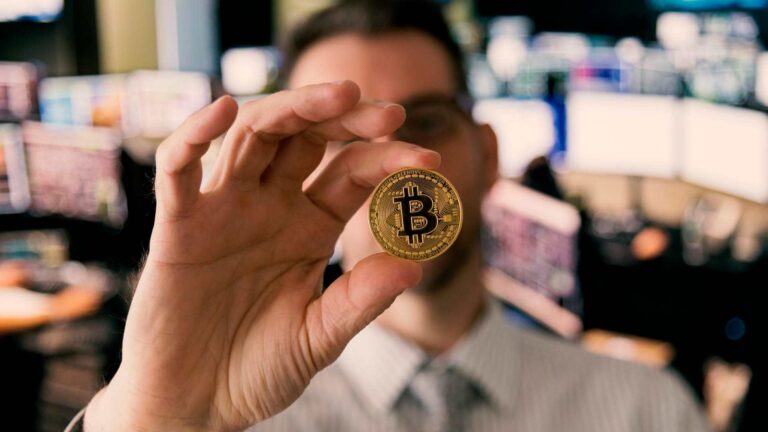 Homem analisando bitcoin com gráficos ao fundo