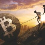 Homem e mulher tentando segurar pedra de bitcoin em montanha Ripio, Mercado Bitcoin e outras corretoras pedem registro no Banco Central antes do prazo final no dia 30 de outubro