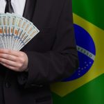 Homem segurando Dólar com bandeira do Brasil ao fundo